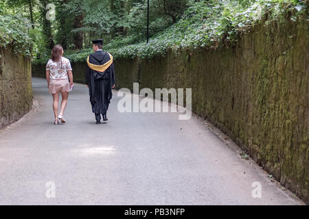 Junge College-Paar gesehen, die einen Campus-Pfad hinunter, nach der Abschlussfeier des jungen Mannes. Stockfoto