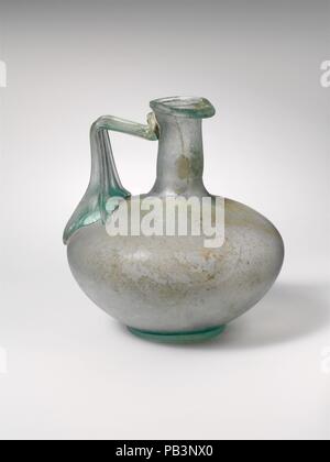 Glaskanne. Kultur: Roman. Abmessungen: H.: 3 3/4 in. (9,5 cm) Durchm.: 1 x 3 3/8 x 1 5/8 in. (2,5 x 8,6 x 4,1 cm). Datum: 1.-2. Jh. N.CHR.. Transluzent blau grün; in gleicher Farbe. Unregelmäßige rim, Ausgeklappt, rund, und in der, teilweise mit abgeschrägten äußeren Lippe; zylindrische Hals; Hocke, bauchigen Körper; feste Basis ring; welligen Boden mit zentralen Kick; zwei gerippte Strap Griff am oberen Gehäuse mit zwei gespreizte Arme an den Seiten und Rippen senkrecht nach unten auszudehnen, und sie sich dann in einem spitzen Winkel gedreht, und drückte auf der Hals nach oben. Intakt; pinprick Blasen, länglich Stockfoto