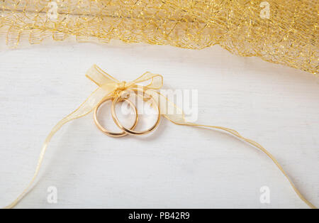 Ein paar goldene Hochzeit Ringe mit einem goldenen Band auf weißen Hintergrund Holz gebunden Stockfoto