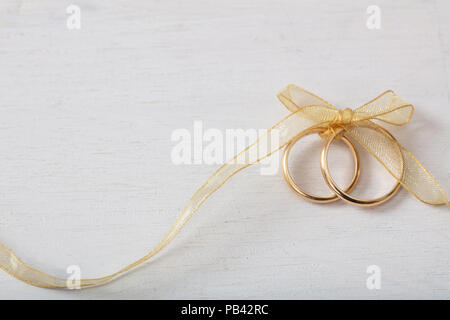 Ein paar goldene Hochzeit Ringe mit einem goldenen Band auf weißen Hintergrund Holz gebunden, kopieren Raum Stockfoto