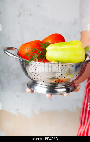 Frau in einem roten Schürze mit einem Sieb mit Gemüse für Salat. Das Kochen. Stockfoto