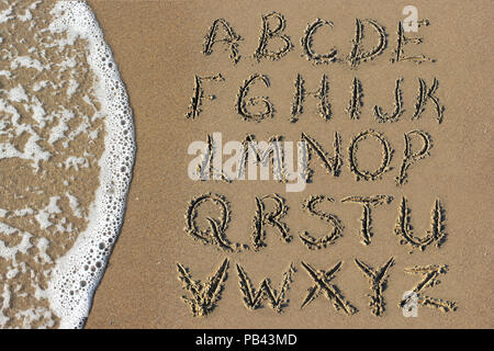 Buchstaben des Alphabets handschriftlich in Sand am Strand Stockfoto