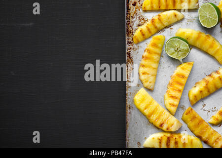 Gegrillte Ananas mit Kalk auf Fach über schwarzer Hintergrund, flach. Von oben, Overhead, Ansicht von oben. Kopieren Sie Raum und Text. Stockfoto