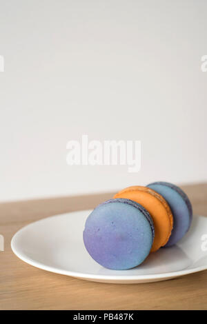 3 Orange und Blau Macarons sitzen auf ihren Seiten auf einem Teller - Vertikal Stockfoto