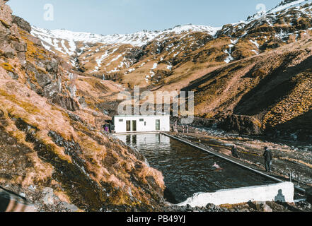 Natürlichen Swimmingpool Seljavallalaug in Island mit Mann in Wasser und Schnee und die Berge rundum. Sonnenschein und blauer Himmel. Stockfoto