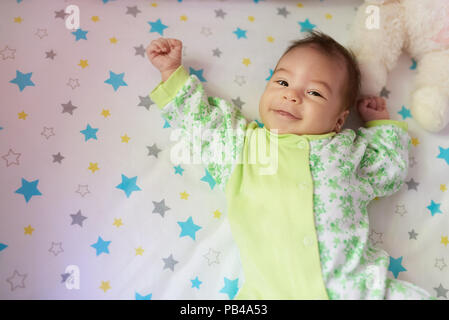 Happy Baby Mädchen mit auf dem Bett mit den Händen bis Stockfoto