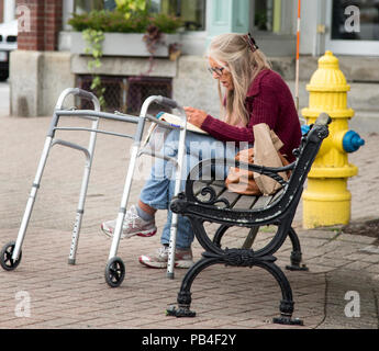 Ältere Frauen sitzen auf einer Bank mit ihrem Walker von ihrer Seite. Stockfoto