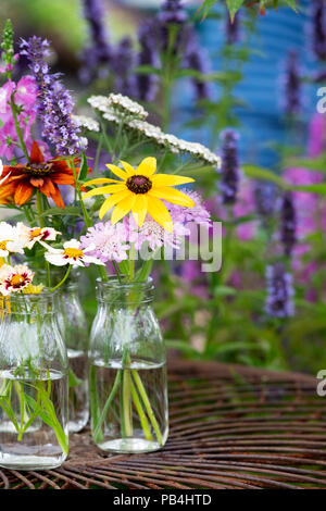 Blumen in Glasflaschen auf ein Metall Garten Tisch eine Blume zeigen. Großbritannien Stockfoto