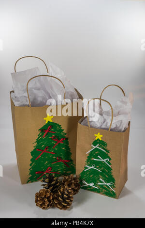 Zwei Papier Geschenktüten für Weihnachten dekoriert und bereit für zusammen mit vier Tannenzapfen Stockfoto