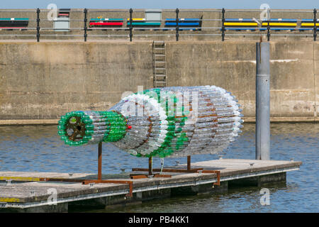 Große übergroße Getränke Flaschenskulptur aus recyceltem, wiederverwendetem, Upcycling-Kunststoff New Brighton, Wallasey. Öffentliche Kunstwerke von Kunststoff-Container aus gebrauchten Flaschen gebaut. Künstler Lulu Quinn schöne und zum Nachdenken anregende „Message in a Bottle“-Upcycling-Flaschenskulptur in Position am Marine Lake. Das 8 m lange Kunstwerk wurde aus 1,500 gebrauchten Getränkeflaschen aus Kunststoff gefertigt, die aus der ganzen Region gesammelt wurden. Stockfoto