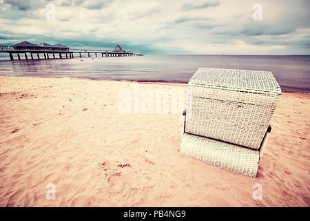 Vintage getonten Bild eines hooded Weidenkorb Stuhl am Strand. Stockfoto