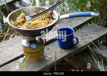 Camping Essen. Pasta auf Pan auf touristische Brand Herd. Camp Kochen am Ufer des Sees. Stockfoto