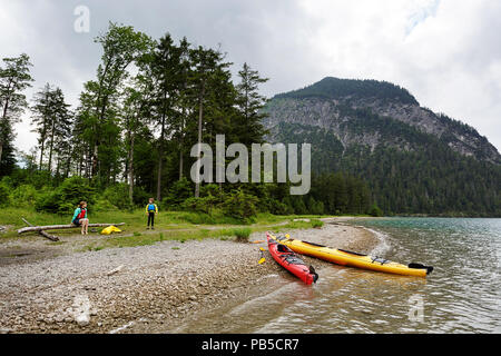Mutter und Sohn mit allen Kajak Ausrüstung auf einem getrockneten Log nach dem Kajakfahren auf am Plansee, Österreich sitzen Stockfoto