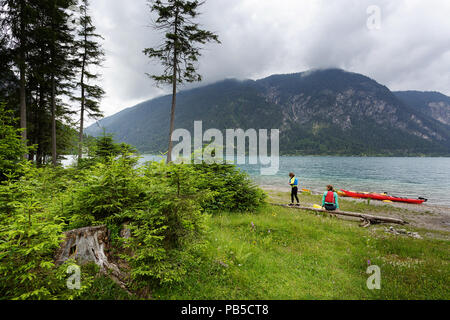 Mutter und Sohn mit allen Kajak Ausrüstung auf einem getrockneten Log nach dem Kajakfahren auf am Plansee, Österreich sitzen Stockfoto