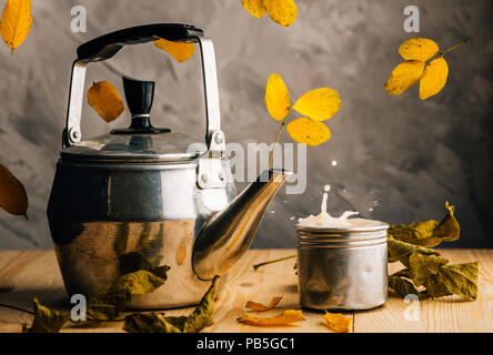 Ahornblätter und heißen Tee in einem Tee Set erstellen Sie eine herbstliche Stimmung. Herabfallendes Laub und Spritzen der Milch Kaffee Stockfoto