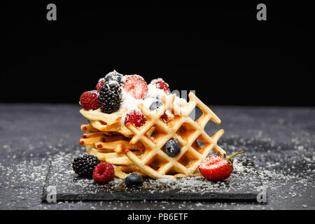 Foto von Wiener Waffeln mit frischen Himbeeren, Erdbeeren bestreut mit Puderzucker auf Tafel gegen leere Hintergrund Stockfoto