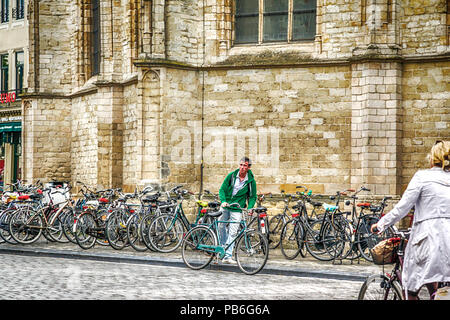 Zwei Menschen auf Fahrrädern, während Dutzende mehr entlang der Backsteinkirche Wand in Breda, Niederlande, EU geparkt Stockfoto