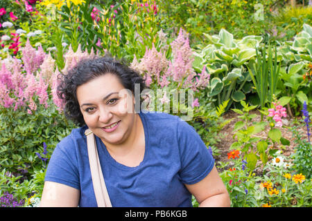 Kopf und Schultern schoss einer Frau stand vor der rosa Blumen in einem Garten Stockfoto