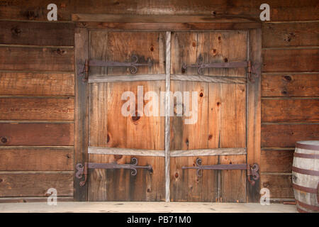 Alte hölzerne Flügeltüren mit rostige verwitterte Hardware, Holzfässer neben Tür gestapelt. Close Up. Stockfoto