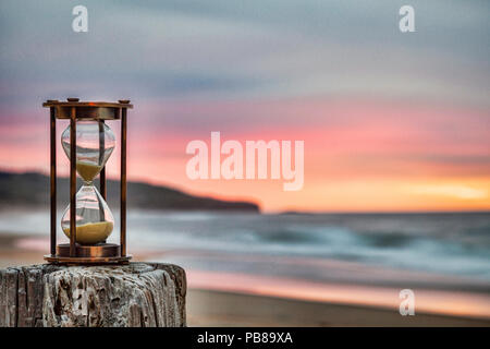 Sanduhr im Freien stehend auf Jetty Post mit stimmungsvollen Sonnenaufgang Himmel. Stockfoto