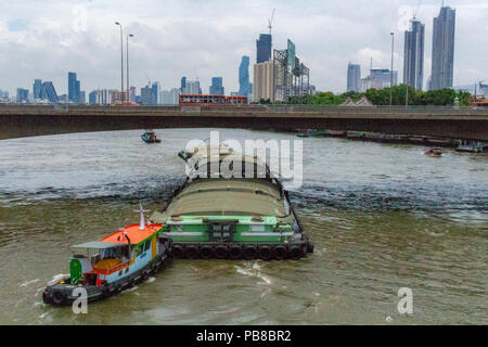 Bangkok, Thailand - 1. Mai 2018: Traction Boot treibt ein Transport Boot über einen Fluss mit Bangkok Skyline im Hintergrund Stockfoto