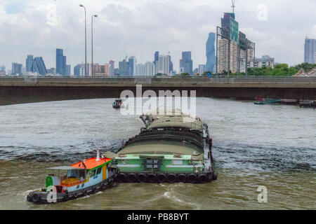 Bangkok, Thailand - 1. Mai 2018: Traction Boot treibt ein Transport Boot über einen Fluss mit Bangkok Skyline im Hintergrund Stockfoto