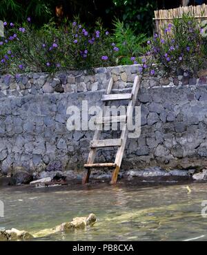 Holzleiter lehnte sich gegen eine Wand an einem See. Stockfoto
