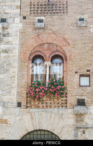 Fenster mit Fensterkreuz mit Blumen auf einem Gebäude in San Gimignano, Toskana, Italien Stockfoto