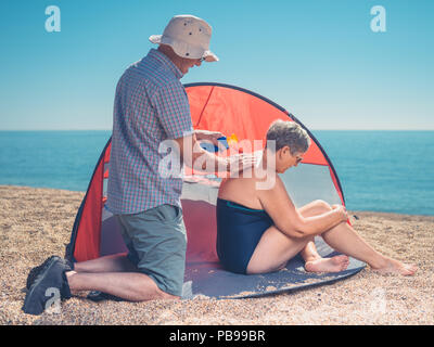Ein älterer Mann ist die Sonnencreme zu seiner Frau zurück Stockfoto