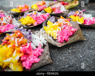 Reihen von hellen Gelb und Rosa Reis Angebote in der Palme treibt auf dem Bürgersteig an Saka Silvester während Nyepi, Nusa Lembongan, Bali, Indonesien Stockfoto