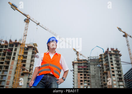 Architekt Stolz lächelnd auf einer Baustelle mit Gebäuden und Krane im Hintergrund Stockfoto