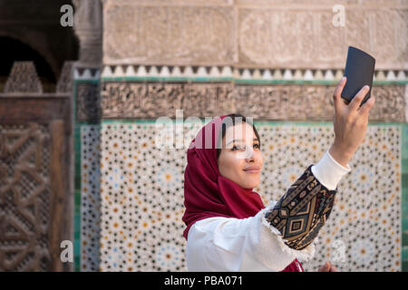 Junge muslimische Frau, die selfie mit Handy in traditioneller Kleidung mit roten Kopftuch Stockfoto