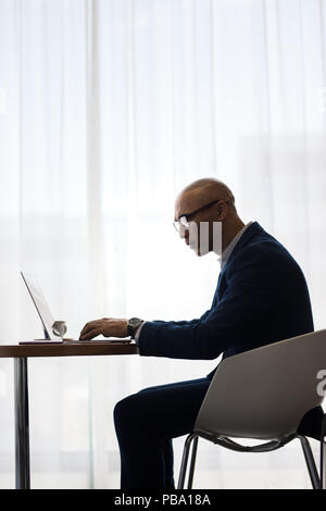 Seitenansicht des Unternehmer sitzen am Tisch und Arbeiten am Laptop im Büro. Unternehmer mit Laptop im Büro. Stockfoto