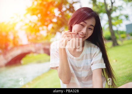Süße asiatische Frau lächeln mit Finger Grübchen Wange im Park Stockfoto