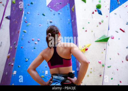 Foto von jungen Athleten Mädchen von hinten mit den Händen auf der Hüfte - neben der Wand zum Klettern in der Turnhalle Stockfoto