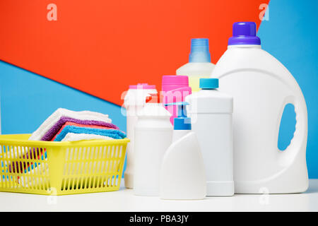 Foto von mehrere Flaschen Reinigungsmittel und bunten Bettwäsche in Korb auf rot, blau, Hintergrund, Platz für die Beschriftung Stockfoto