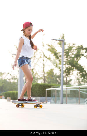 Fröhlicher junger chinesische Frau Skateboarding Stockfoto