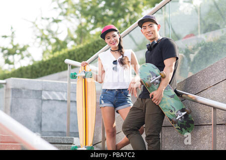 Portrait von fröhlichen jungen chinesischen Paar mit Skateboard Stockfoto