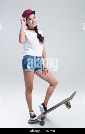 Fröhlicher junger chinesische Frau Skateboarding Stockfoto