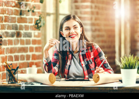 Junge ziemlich lange Haare weiblichen Architekten halten Sie Ihre Brille und lächelnd auf dem Dachboden moderne Büro Stockfoto