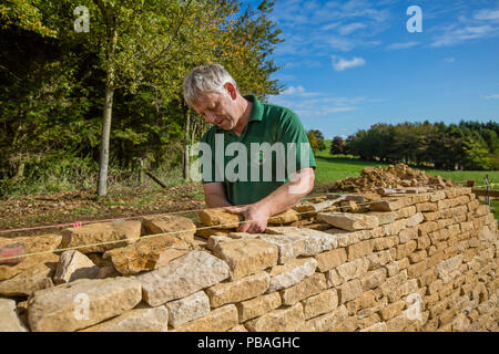 Traditionelle Trockenmauern Waller arbeiten mit Cotswolds Kalkstein eine Mauer, Guiting Macht, Gloucestershire, Vereinigtes Königreich. Oktober 2015. Stockfoto