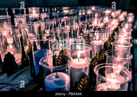 Closeup Seite Muster von vielen weißen, blauen religiösen Votiv Kerzen mit gelben, violetten Flamme in Kirche oder Kathedrale Stockfoto