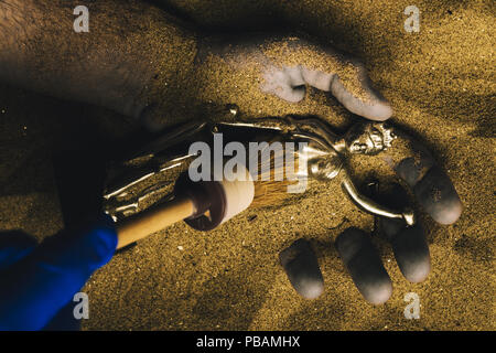 Forensische Experten entdecken Leiche in der Wüste Sand mit Gerechtigkeit Statue in der Hand begraben. Konzeptionelle Bild für die polizeiliche Untersuchung eines kalten Fall mur Stockfoto