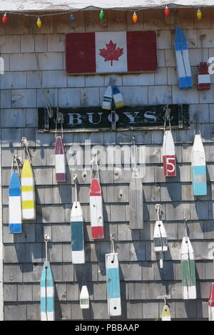 Nahaufnahme von bunten Bojen an der Wand aufhängen, unter einem Schild mit der Aufschrift "BOJEN" und der kanadische Maple Leaf Flag; North Rustico, PEI Stockfoto