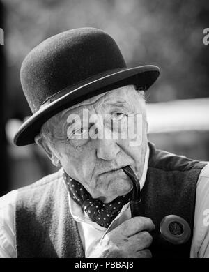 Schwarz-Weiß-Frontansicht Porträt, älterer Mann in schwarzem Melone Hut rauchende Pfeife, tief in Gedanken, ernsthaft ernst: Großbritannien 1940er Jahre. Stockfoto