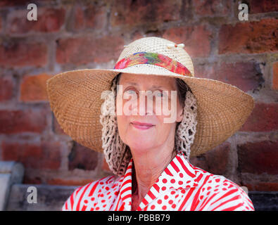 Nahaufnahme, Vorderansicht Porträt einer isolierten Seniorin, Haar in gestricktem Schlauchschal mit breiter Krempe, weiträumiger Strohhut, Sommerveranstaltung der 40er Jahre, Großbritannien. Stockfoto