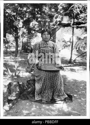 . Englisch: Paiute indische Frau korbmacher von Yosemite Valley, Ca. 1900 Foto der Paiute indische Frau korbmacher von Yosemite Valley, Ca. 1900. Sie sitzt auf einem Stuhl oder Hocker mit einem großen flachen Korb in ihrem Schoß. Sie ist in einem langen Kleid mit einem Riemen gekleidet. Ein Hund sitzt auf dem Boden neben ihr auf der linken Seite. Die Gegend ist mit Schatten von den Bäumen hinter ihr gesprenkelt. Rufnummer: CHS-3838 Fotograf: Pierce, C.C. (Charles C.), 1861-1946 Dateiname: CHS-3838 Abdeckung Datum: ca. 1900 Teil der Sammlung: California Historical Society Collection, 1860-1960 Format: Glasplatte Stockfoto