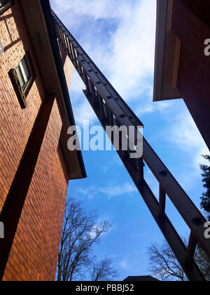 Zwischen zwei angrenzenden Häusern ist eine Verlängerungsleiter für Reparaturen am Dach, Ontario, Kanada, eingerichtet. Blick vom Boden nach oben. Stockfoto