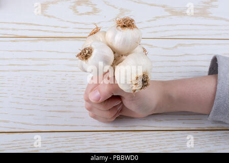 Hand, die Knoblauchzehen auf einer hölzernen Textur Stockfoto