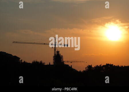 Die Silhouetten von zwei Kränen in die Stadt bei Sonnenuntergang Stockfoto